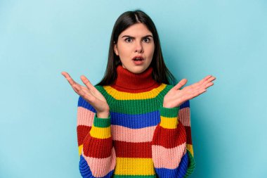 Mavi arka planda izole edilmiş genç beyaz kadın şaşırdı ve şok oldu..