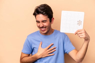 Kafkasyalı genç bir adam bej arka planda izole edilmiş bir yapboz tutuyor. Gülüyor ve eğleniyor..