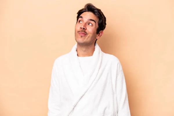 Jonge Blanke Man Draagt Een Badjas Geïsoleerd Beige Achtergrond Dromen — Stockfoto