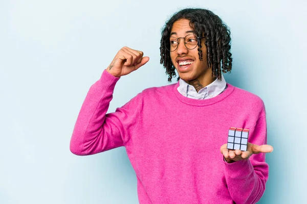 Mladý Afroameričan Drží Kostku Rubiks Izolovanou Modrém Pozadí Zvedající Pěst — Stock fotografie