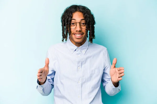 Joven Afroamericano Aislado Sobre Fondo Azul Sosteniendo Algo Con Ambas —  Fotos de Stock