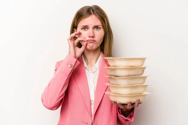 Young business English woman holding tupperware of food isolated on white background with fingers on lips keeping a secret.