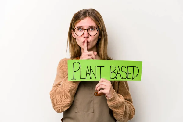 Young gardener woman holding a plan based placard isolated on white background keeping a secret or asking for silence.