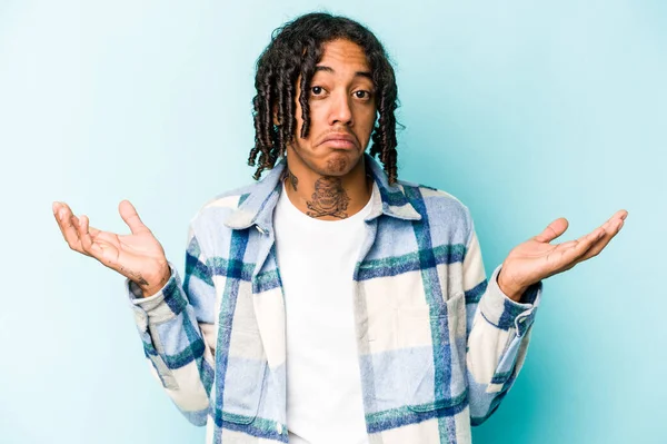 Genç Afrikalı Amerikalı adam mavi arka planda izole edilmiş sorgulama jestinde şüphe ediyor ve omuz silkiyor..