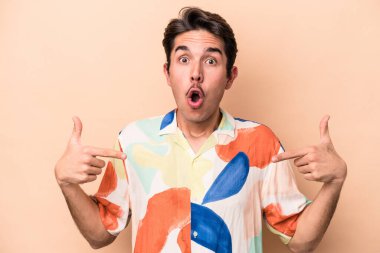 Beyazlı genç bir adam bej arka planda izole edilmiş. Parmakları aşağıda, olumlu hisler içinde..