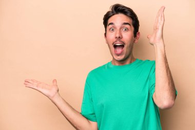 Beyazların arka planında izole edilmiş genç beyaz bir adam bir avuç içinde fotokopi alanı tutuyor, el üstünde tutuyor. Şaşırmış ve mutlu..