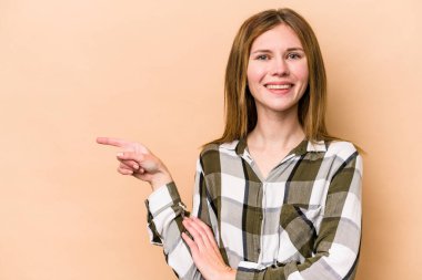 Bej arka planda izole edilmiş genç bir İngiliz kadın işaret parmağıyla işaret ederek gülümsüyor..