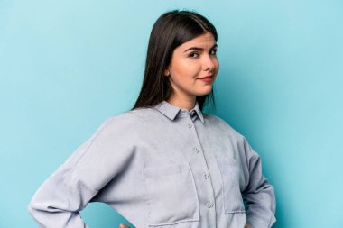 Mavi arka planda izole edilmiş genç beyaz kadın hoşnutsuzca kaşlarını çatmış, kollarını kavuşturmuş..