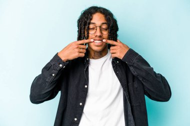 Genç Afrikalı Amerikalı adam mavi arka planda izole edilmiş gülümsüyor, parmaklarını ağıza doğrultuyor..