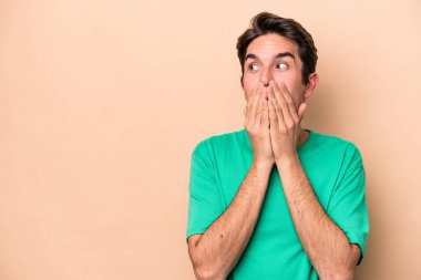 Beyazlı genç bir adam bej arka planda izole edilmiş. Düşünceli bir şekilde bir fotokopi odasına bakıyor. Ağzını eliyle kapatıyor..