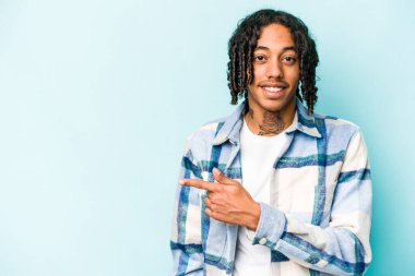 Genç Afrikalı Amerikalı adam mavi arka planda izole edilmiş gülümsüyor ve boş alanda bir şeyler gösteriyor..