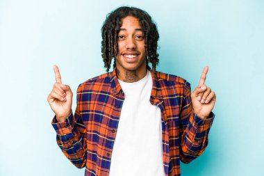 Mavi arka planda izole edilmiş genç Afrikalı Amerikalı iki parmağı da boş bir alan gösteriyor..