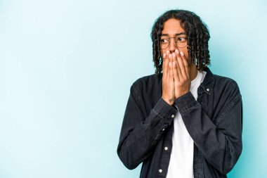 Genç Afrikalı Amerikalı bir adam mavi arka planda izole edilmiş. Düşünceli bir şekilde bir fotokopi odasına bakıyor. Ağzını eliyle kapatıyor..