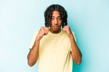 Genç Afrikalı Amerikalı bir adam mavi arka planda izole edilmiş. Bir tartışma yüzünden yumruk, öfke ve kavga atıyor..