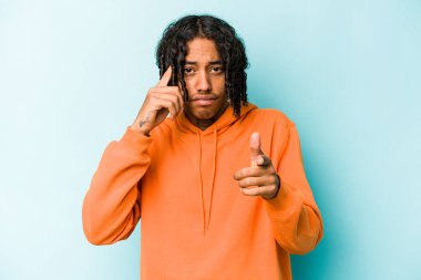Genç Afrikalı Amerikalı bir adam mavi arka planda izole edilmiş. Parmağıyla tapınağı işaret ediyor. Düşünüyor, bir göreve odaklanıyor..