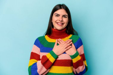 Mavi arka planda izole edilmiş beyaz bir kadın, dost canlısı bir ifadeye sahip, avuçlarını göğsüne bastırıyor. Aşk konsepti.