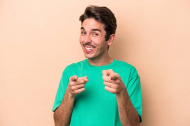 Beyazların arka planında izole edilmiş genç beyaz adam parmaklarıyla ön tarafı işaret ediyor..