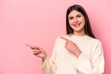 Pembe arka planda izole edilmiş genç beyaz kadın işaret parmaklarıyla işaret ederek heyecanlanıyor..