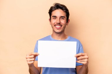 Beyazlı genç bir adam bej arka planda izole edilmiş bir pankart tutuyor. Mutlu, gülümseyen ve neşeli..