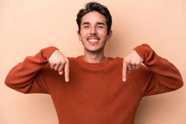 Beyazlı genç bir adam bej arka planda izole edilmiş. Parmakları aşağıda, olumlu hisler içinde..