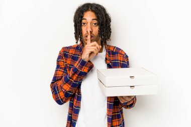 Mavi arka planda izole edilmiş pizzalar tutan genç Afrikalı Amerikalı bir adam sır saklıyor ya da sessizlik istiyor..