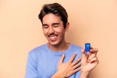 Beyazlı genç bir adam bej arka planda izole edilmiş bir bateri tutuyor. Gülüyor ve eğleniyor..