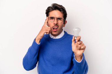 Beyaz arka planda izole edilmiş bir ampul tutan genç beyaz bir adam işaret parmağıyla hayal kırıklığı jesti gösteriyor..