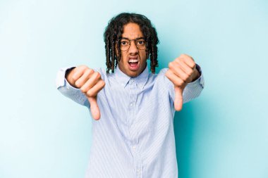 Genç Afro-Amerikalı adam mavi arka planda izole edilmiş baş parmağını aşağı gösteriyor ve hoşlanmadığını ifade ediyor..