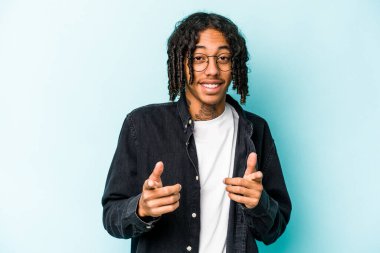 Genç Afrikalı Amerikalı, mavi arka planda izole edilmiş, parmaklarıyla ön tarafı işaret ediyor..