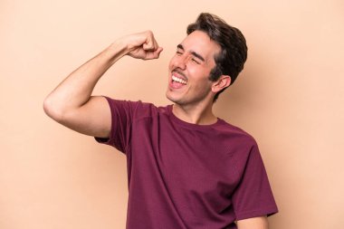 Beyazlı genç adam bej arka planda izole edilmiş zafer, tutku ve coşkuyu kutluyor, mutlu bir ifade..