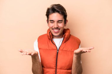 Beyaz tenli genç adam bej arka planda izole edilmiş. Elinde avuç içi olan bir şeyle kameraya sunuyor..