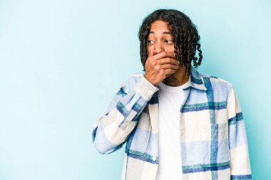 Genç Afrikalı Amerikalı bir adam mavi arka planda izole edilmiş. Düşünceli bir şekilde bir fotokopi odasına bakıyor. Ağzını eliyle kapatıyor..