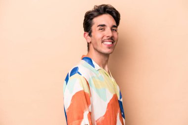 Beyaz tenli genç adam bej arka planda izole edilmiş. Kendine güveniyor. Kalçaları tutuyor..