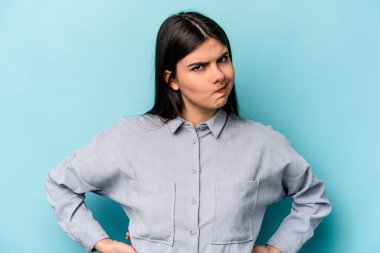 Kafkasyalı genç bir kadın mavi arka planda izole edilmiş, kafası karışmış, şüpheli ve kendinden emin değil..