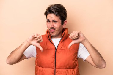 Beyazlı genç adam bej arka planda izole edilmiş baş parmağını aşağı gösteren, hayal kırıklığı konsepti.