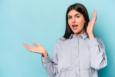 Mavi arka planda izole edilmiş beyaz bir kadın avuç içinde fotokopi alanı tutuyor, el üstünde tutuyor. Şaşırmış ve mutlu..