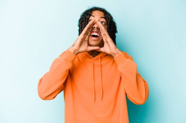 Genç Afrikalı Amerikalı adam mavi arka planda izole edilmiş ve heyecanlı bir şekilde bağırıyor..