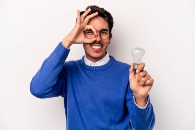 Beyaz arka planda izole edilmiş bir ampul tutan genç beyaz bir adam heyecanlı..