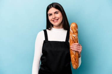 Genç fırıncı Kafkas elinde mavi arka planda izole edilmiş bir somun ekmek tutuyor mutlu, güler yüzlü ve neşeli.