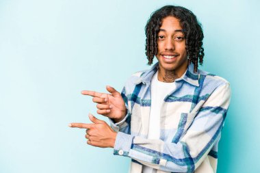 Genç Afro-Amerikalı adam mavi arka planda izole edilmiş. İşaret parmaklarıyla işaret ederek heyecanlı..