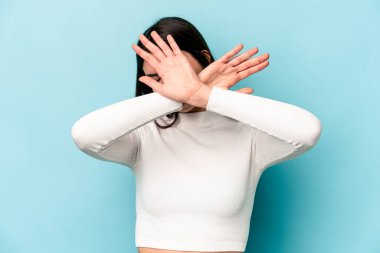 Mavi arka planda izole edilmiş genç beyaz kadın iki kolu çapraz tutuyor, inkar kavramı.