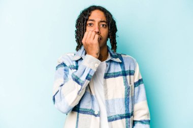 Genç Afrikalı Amerikalı bir adam mavi arka planda izole edilmiş tırnak yiyor, gergin ve çok endişeli..