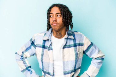 Genç Afrikalı Amerikalı bir adam mavi arka planda izole edilmiş, kafası karışmış, şüpheli ve güvensiz hissediyor..