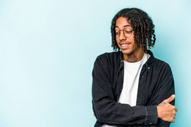 Genç Afrikalı Amerikalı adam mavi arka planda izole edilmiş kollarını kavuşturarak gülümsüyor..