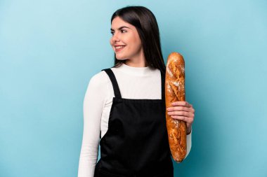 Mavi arka planda izole edilmiş bir somun ekmek tutan genç bir fırıncı gülümseyen, neşeli ve keyifli görünüyor..