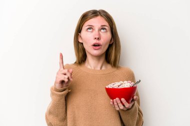 Beyaz arka planda izole edilmiş mısır gevreği yiyen genç bir İngiliz kadın ağzı açık bir şekilde üst tarafı işaret ediyor..