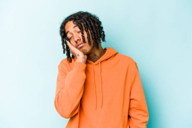 Mavi arka planda izole edilmiş, sıkılmış, yorgun ve dinlenmeye ihtiyacı olan genç Afrikalı Amerikalı bir adam..