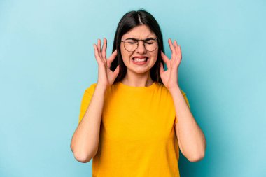Mavi arka planda izole edilmiş genç beyaz kadın kulaklarını elleriyle kapatıyor..