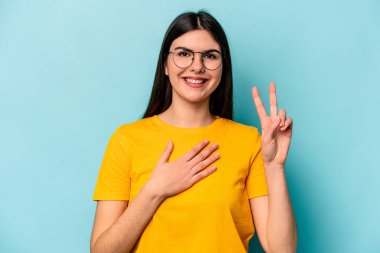 Beyaz bir kadın mavi arka planda izole edilmiş yemin ediyor, elini göğsüne koyuyor..