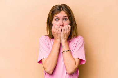 Genç İngiliz kadın bej arka planda izole edilmiş tırnak yiyor, gergin ve çok endişeli..